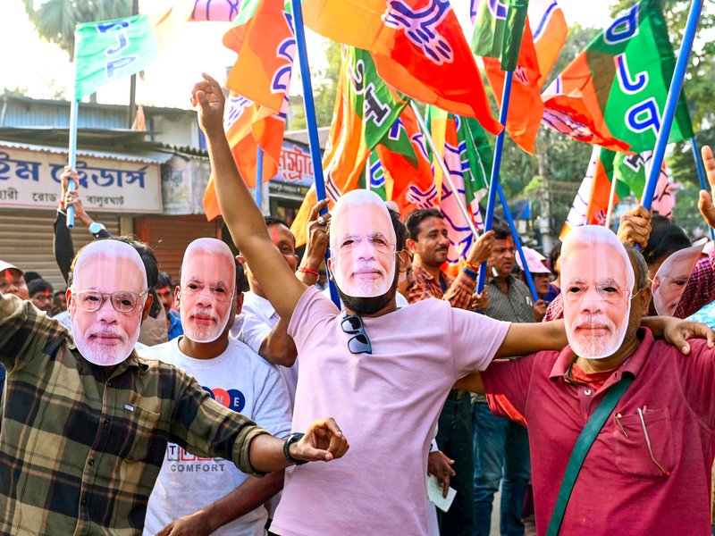 BJP workers wearing masks of Prime Minister Narendra Modi celebrate the party’s victory in the Bihar Assembly elections at Balurghat in the Dakshin Dinajpur district of West Bengal on Friday, November 14, 2025. (Photo: IANS)